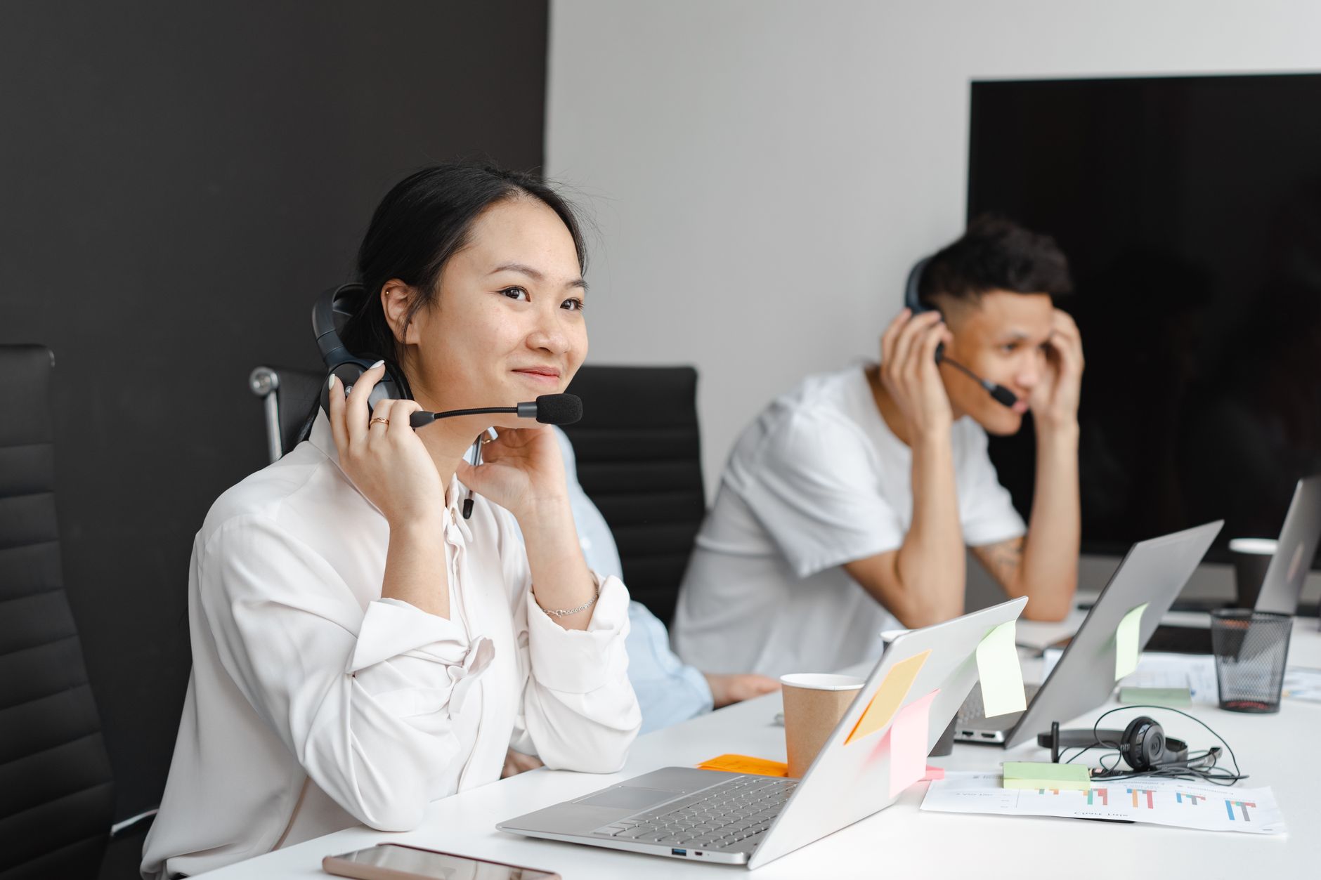 a customer support agent wearing a headset and smiling while looking at a laptop in a modern office