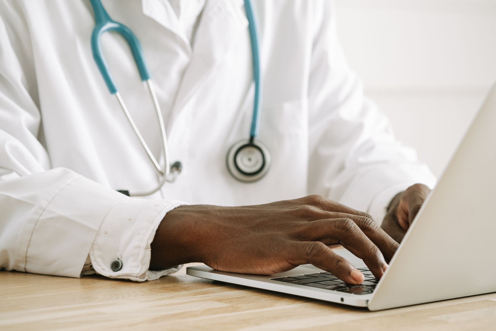 doctor typing notes on a laptop in a clinic while wearing a stethoscope