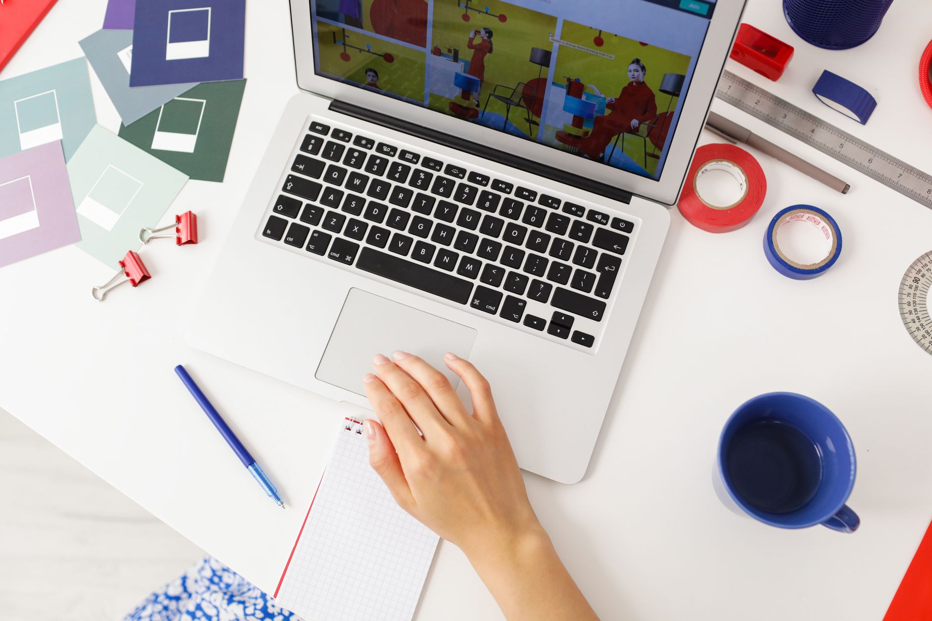 graphic designer creating an invitation layout on a laptop with color swatches on desk