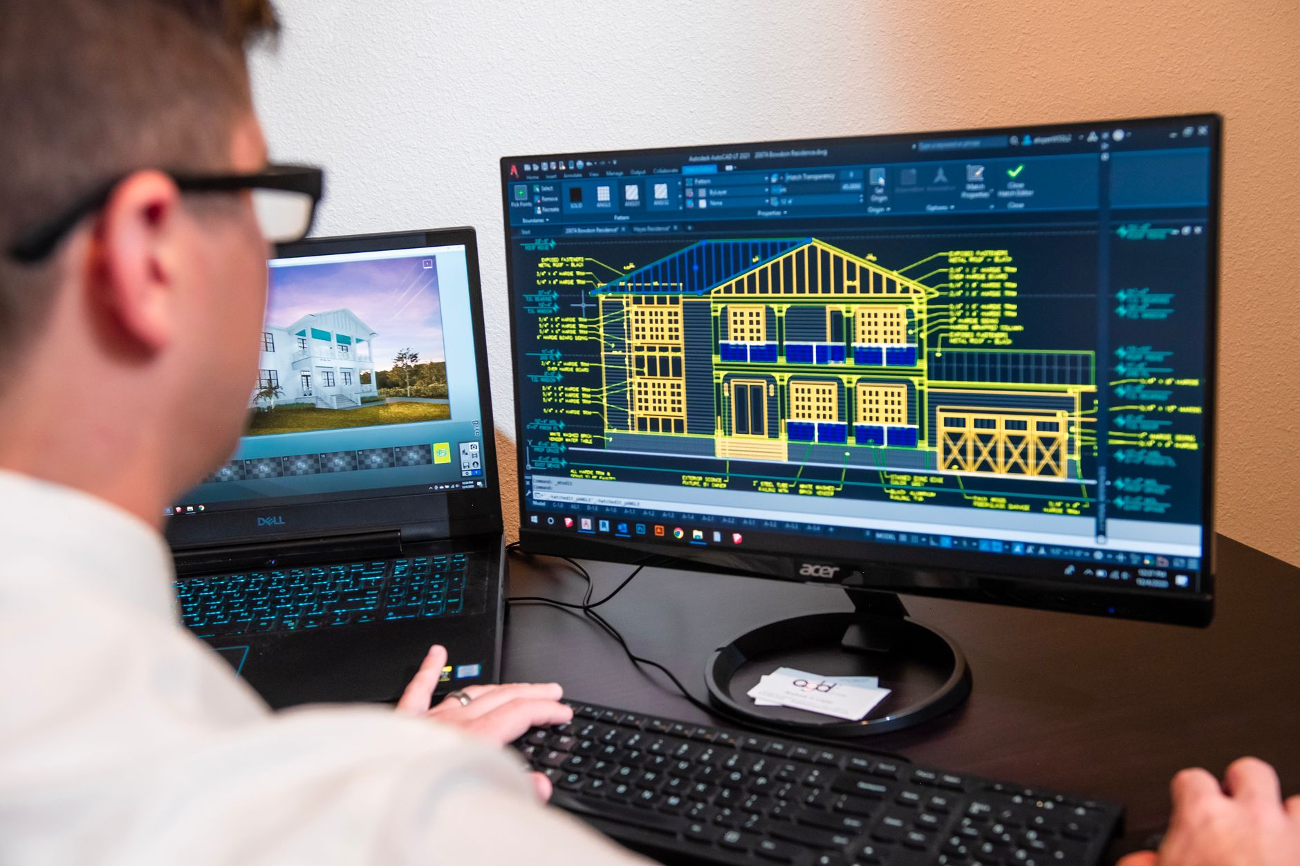 An architect draws a floor plan on a large screen that shows a 3D room model.