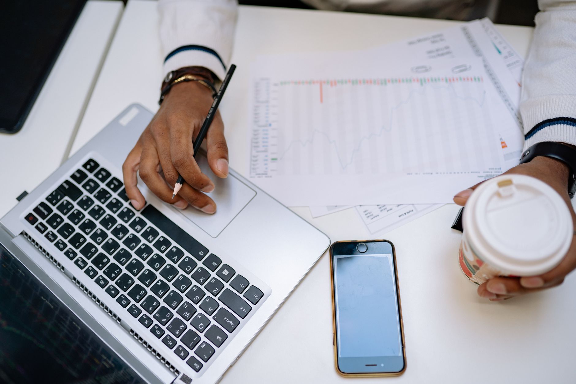 a person sitting at a desk reviewing invoice documents on a laptop with a cup of coffee