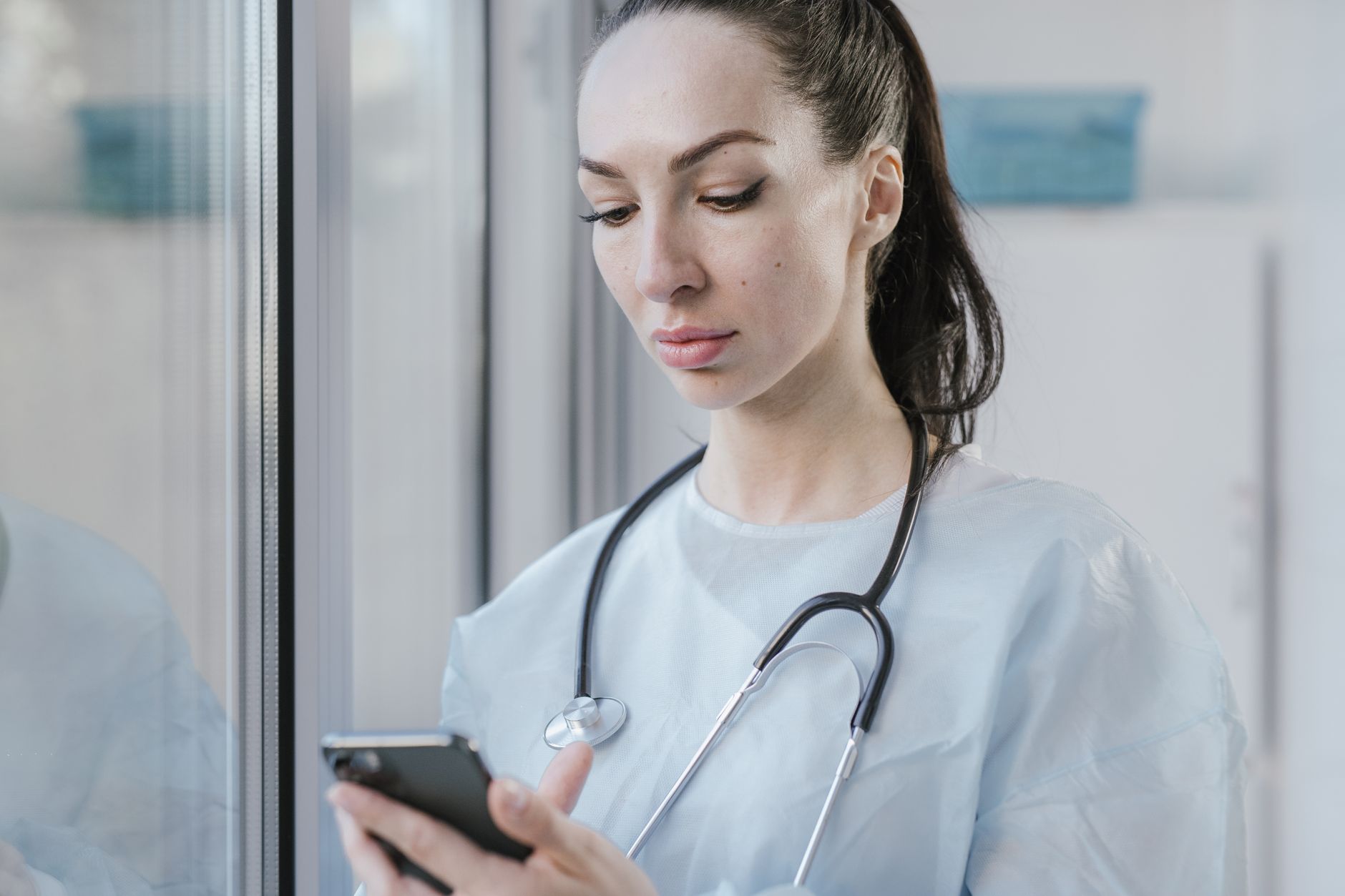 a healthcare worker holding a smartphone with a voice recording app open in a clinic hallway