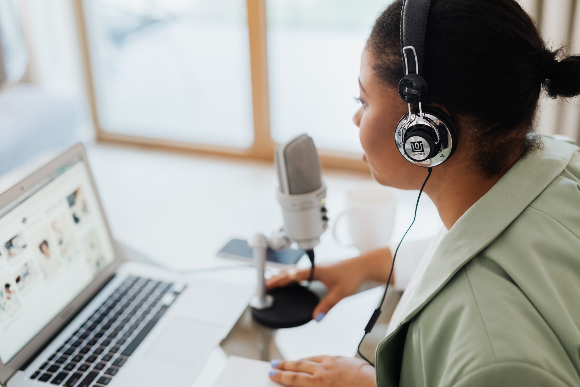 a podcaster wearing headphones and editing audio on a laptop with a microphone on the desk