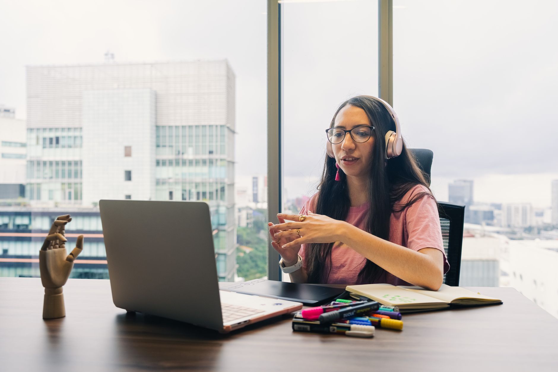 a laptop showing a team video call with a person taking notes and wearing headphones