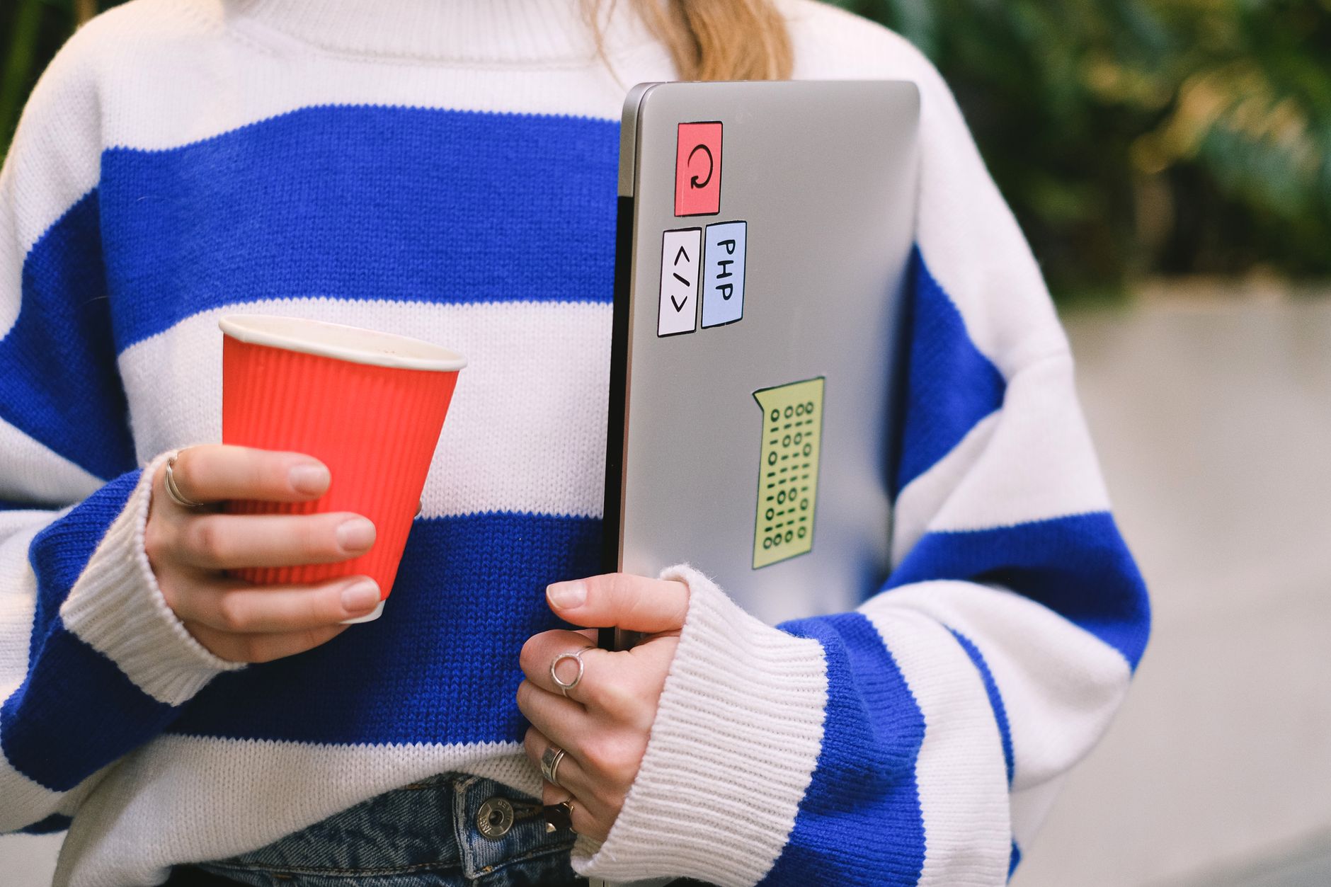 A person looking at a color-coded calendar on a laptop screen while holding a coffee cup