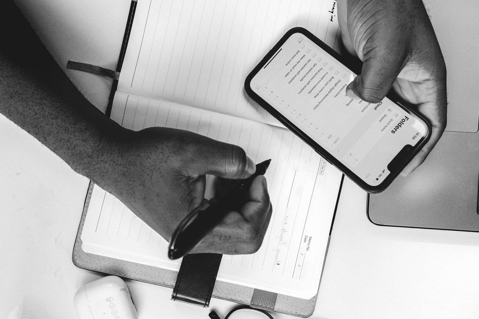 A person using a task management app on a smartphone next to a notebook at a desk