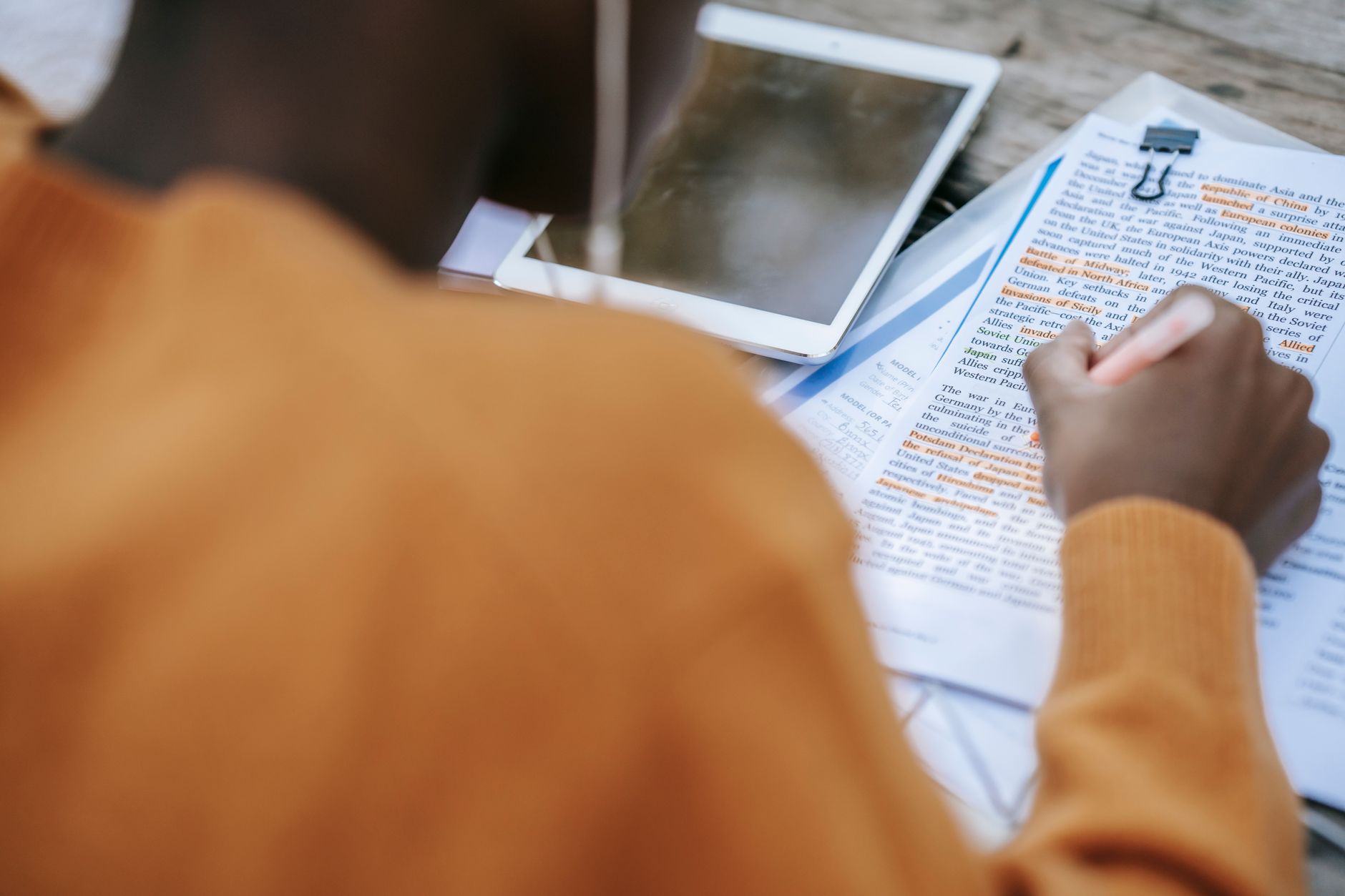student highlighting a paper textbook and taking notes on a tablet