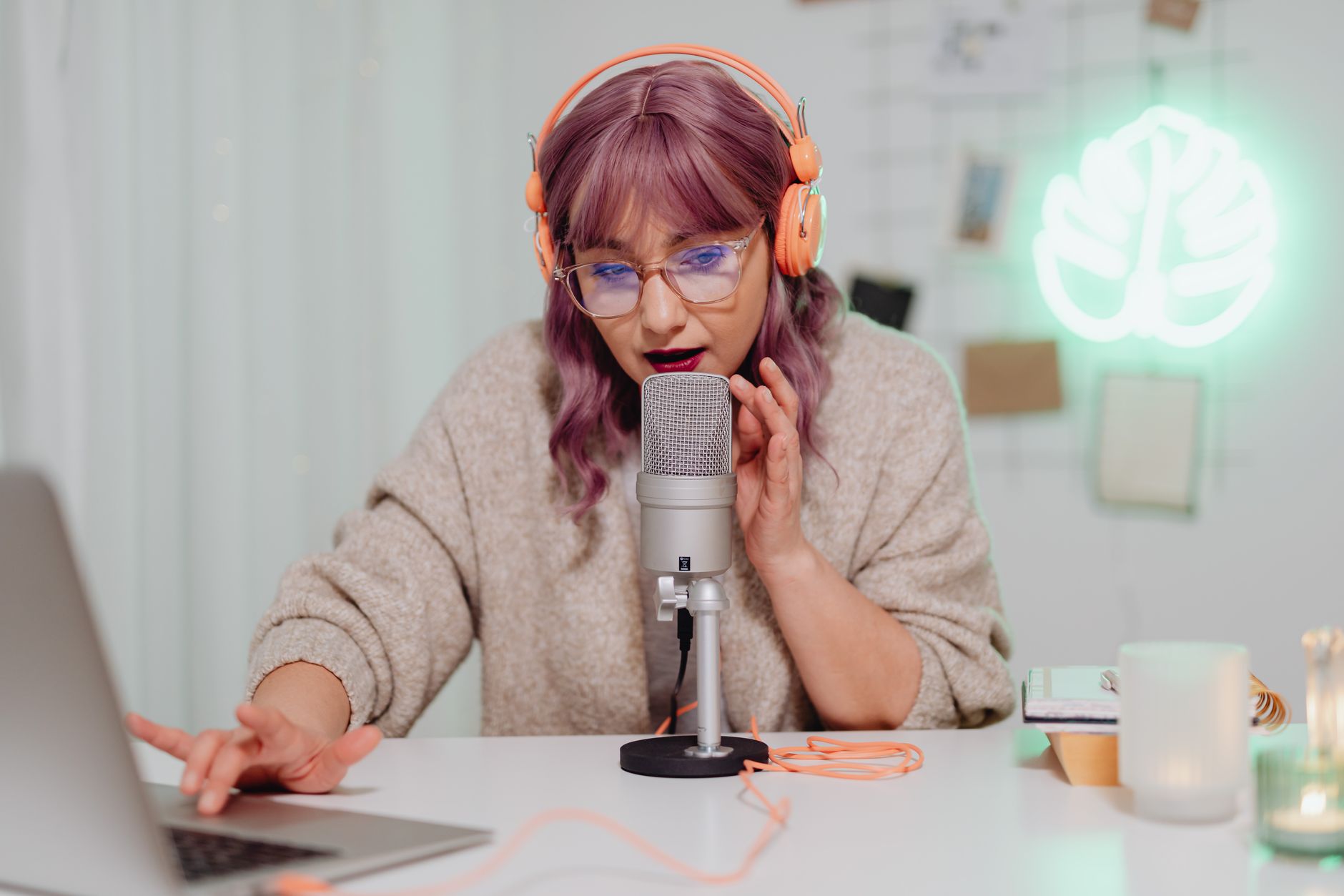 Person wearing headphones speaks into a microphone while editing audio on a laptop