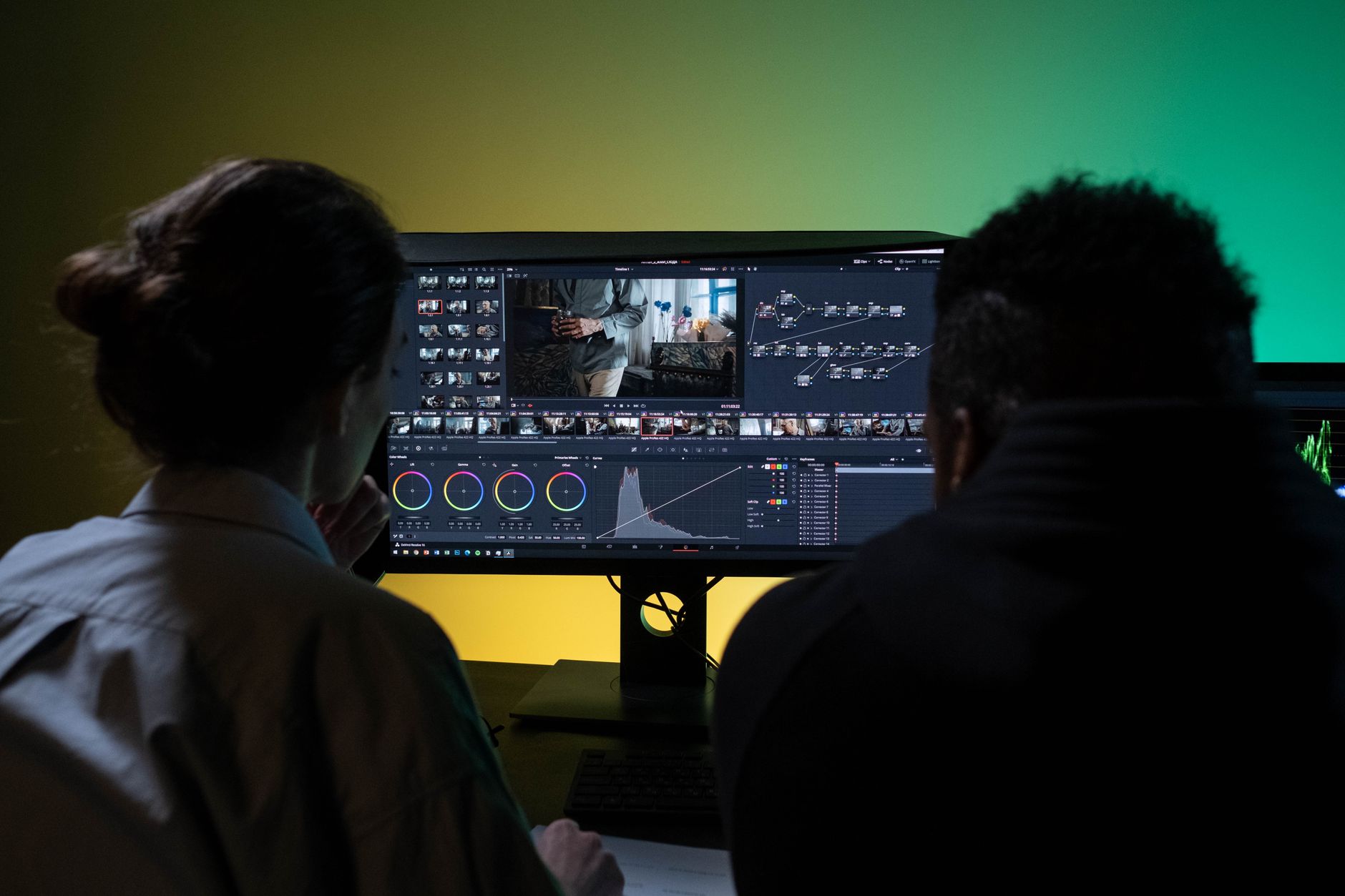 Two people review a voiceover video timeline on a large monitor