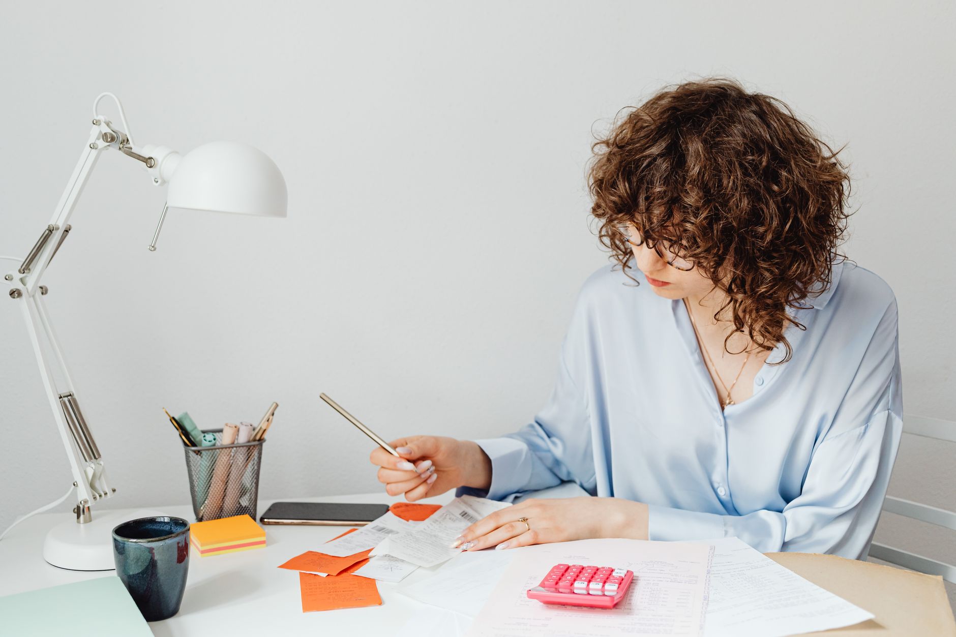 A person holds a phone over a paper receipt at a desk with a laptop and credit cards nearby.