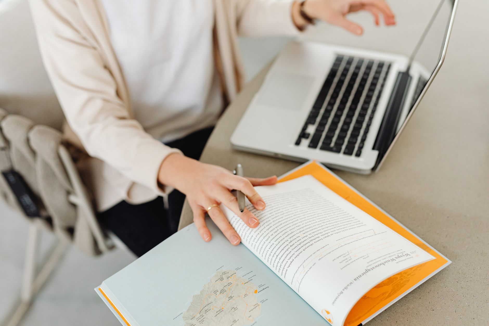 a researcher reading a printed academic paper while typing structured notes on a laptop