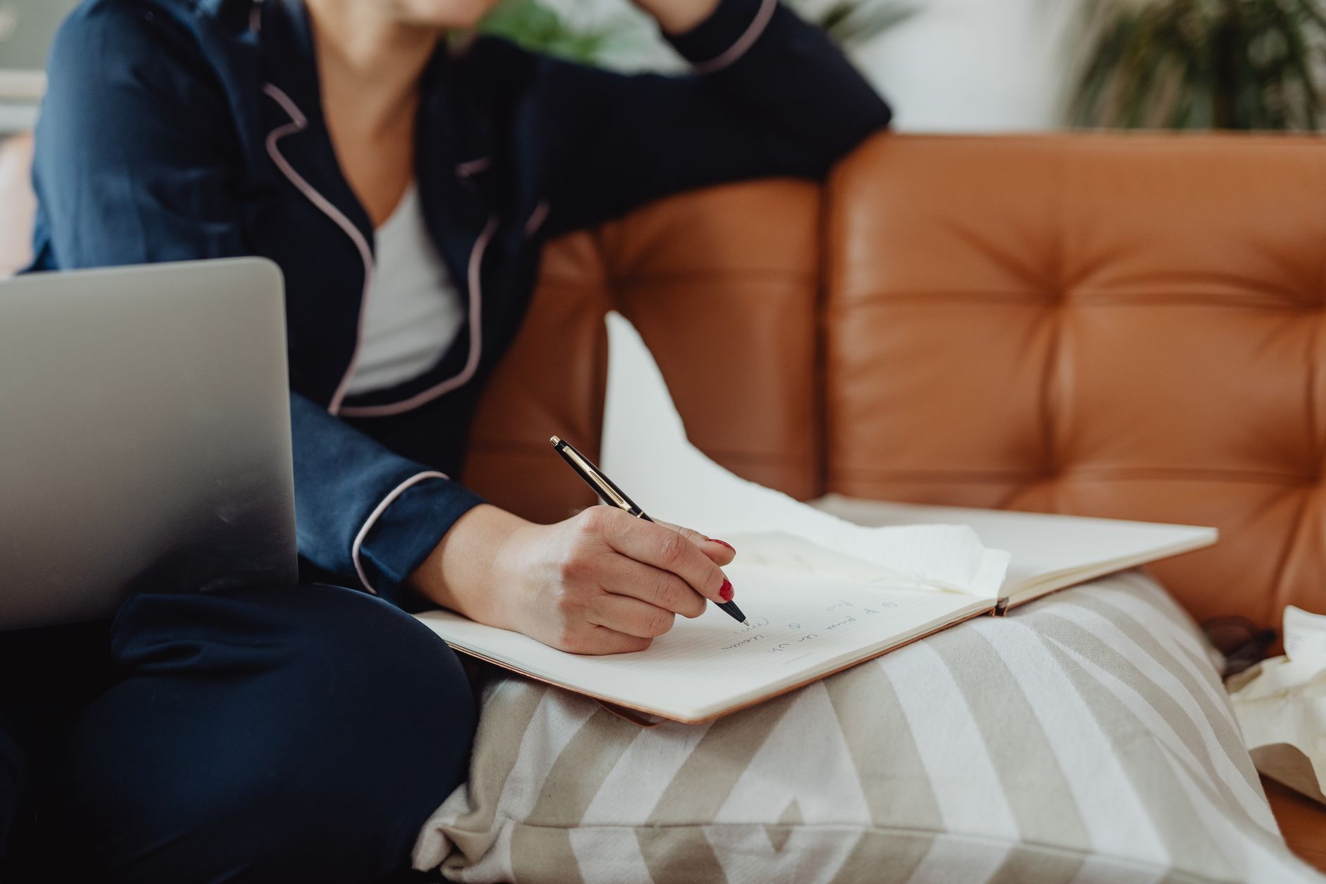 Person writing notes on a laptop in a quiet room with a notebook